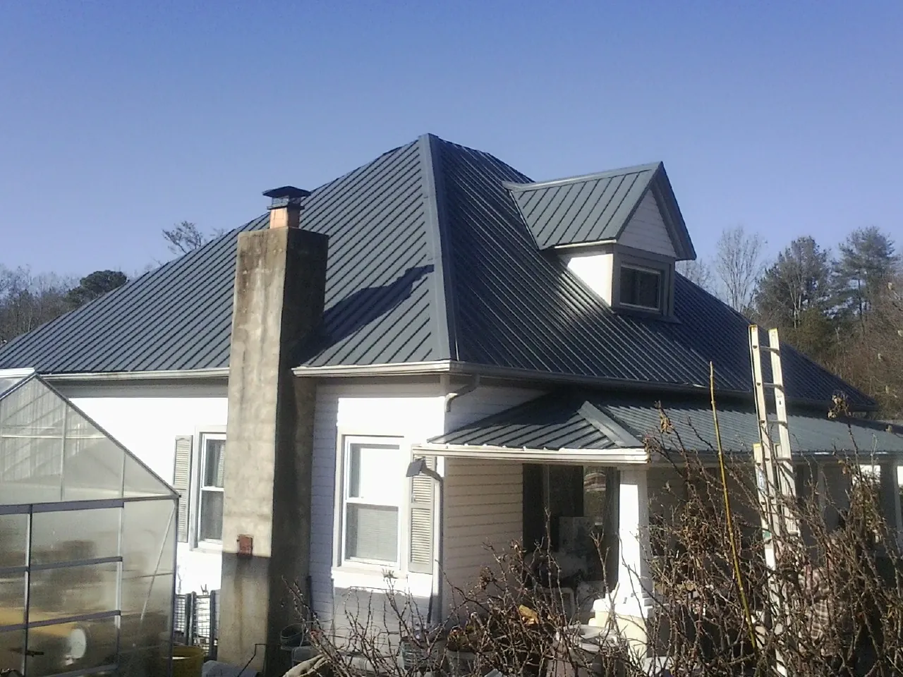 Dark blue standing seam metal roof on a white farmhouse with dormer — Slate & Tile Roof Repair by Roofing Brothers in South Londonderry