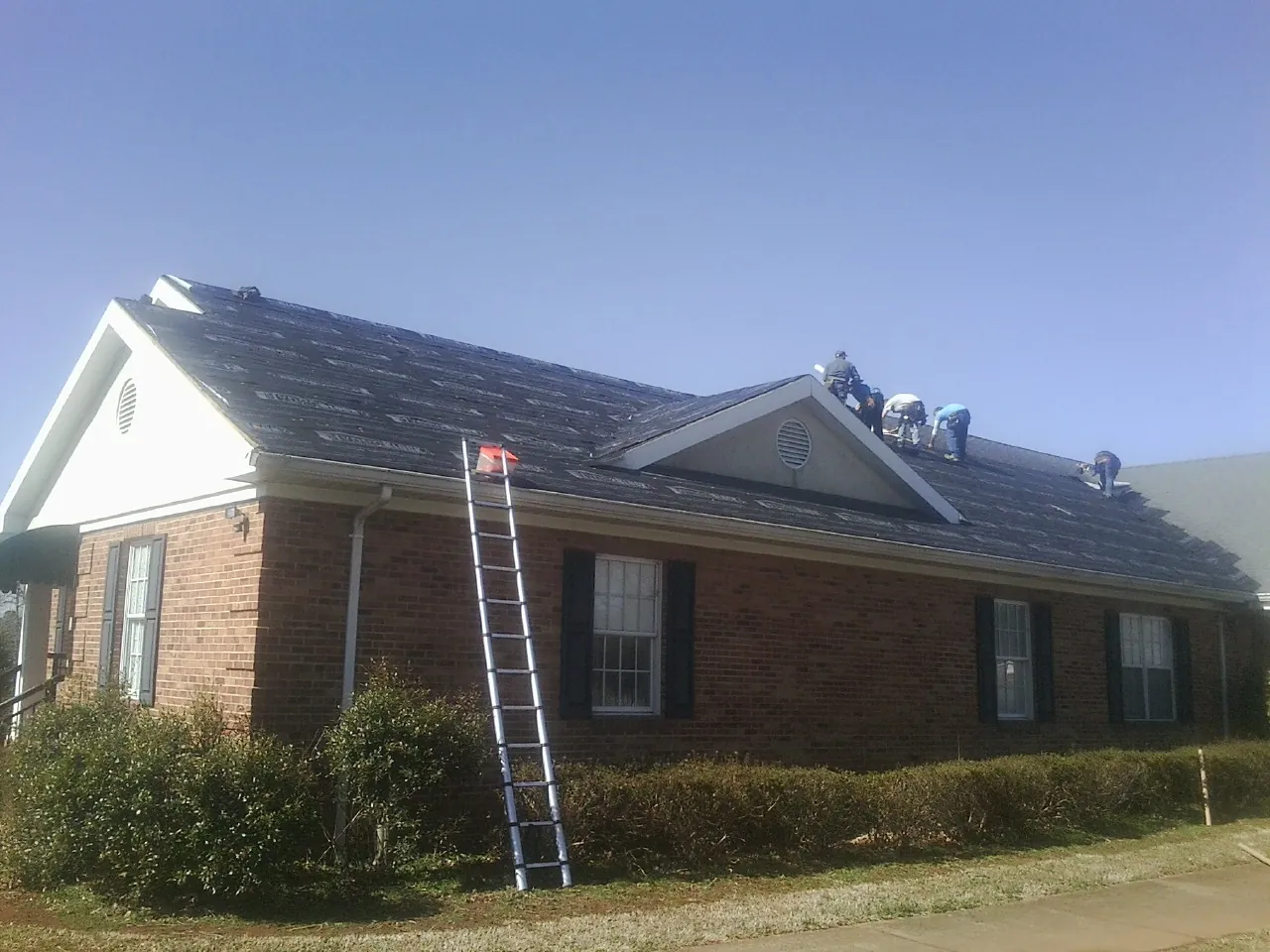 Crew tearing shingles off a brick ranch roof with a ladder set — Emergency Roof Repair work by our crew in South Londonderry