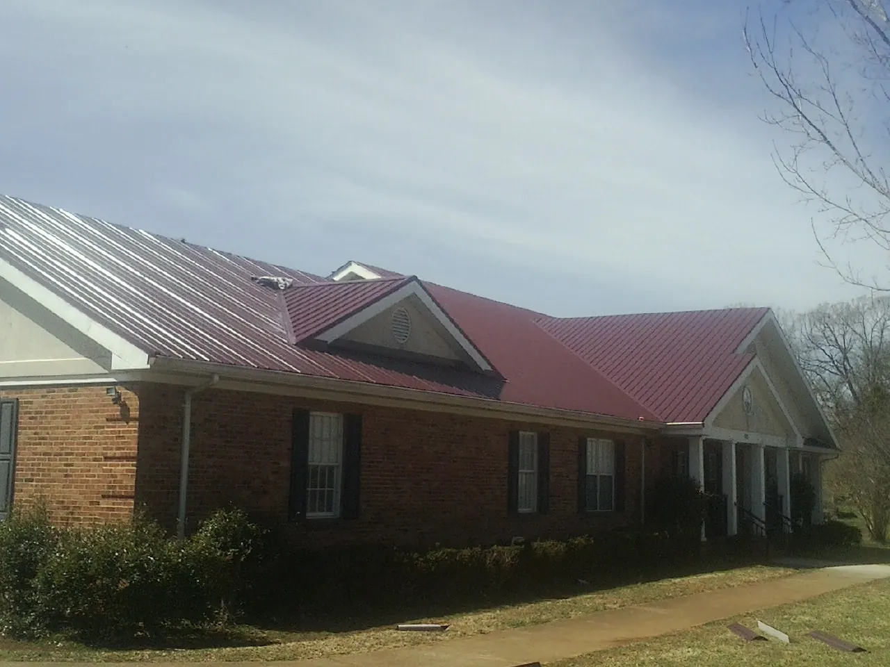 Red metal roof with gabled entries on a long brick building, from a Hail Damage Roof Repair job in South Londonderry