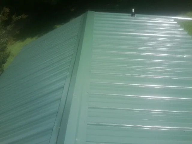 New green metal panels meeting at the ridge of a roof — Flat Roof Repair work by our crew in South Londonderry