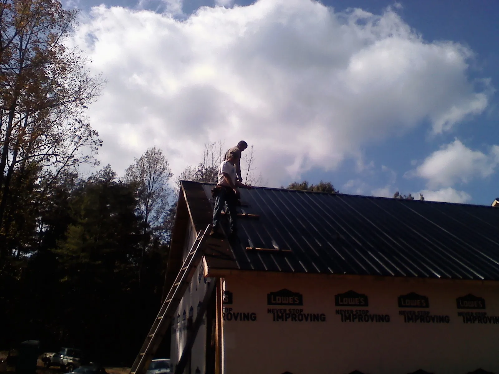 Roofer fastening dark metal panels high against a cloudy sky, from a Roof Inspection job in South Londonderry