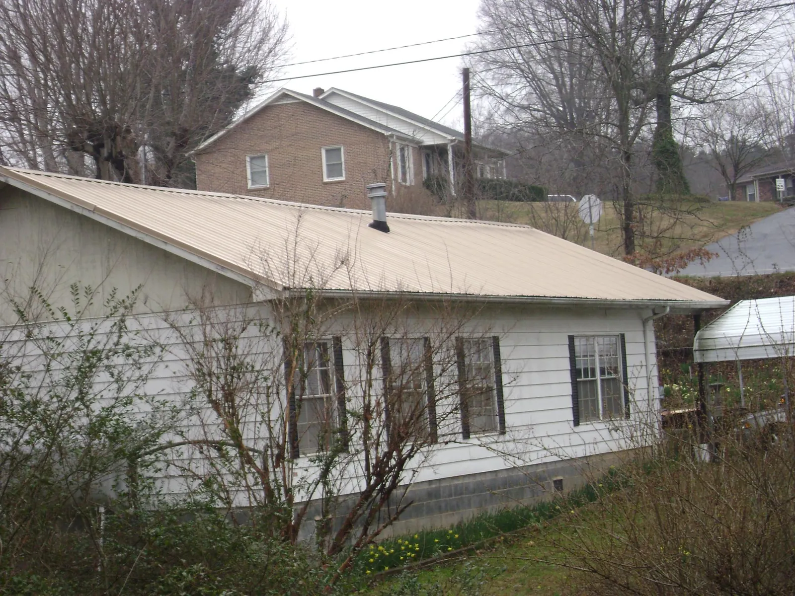 Tan metal roof on a white sided house set into a hillside — Commercial Roofing by Roofing Brothers in South Londonderry